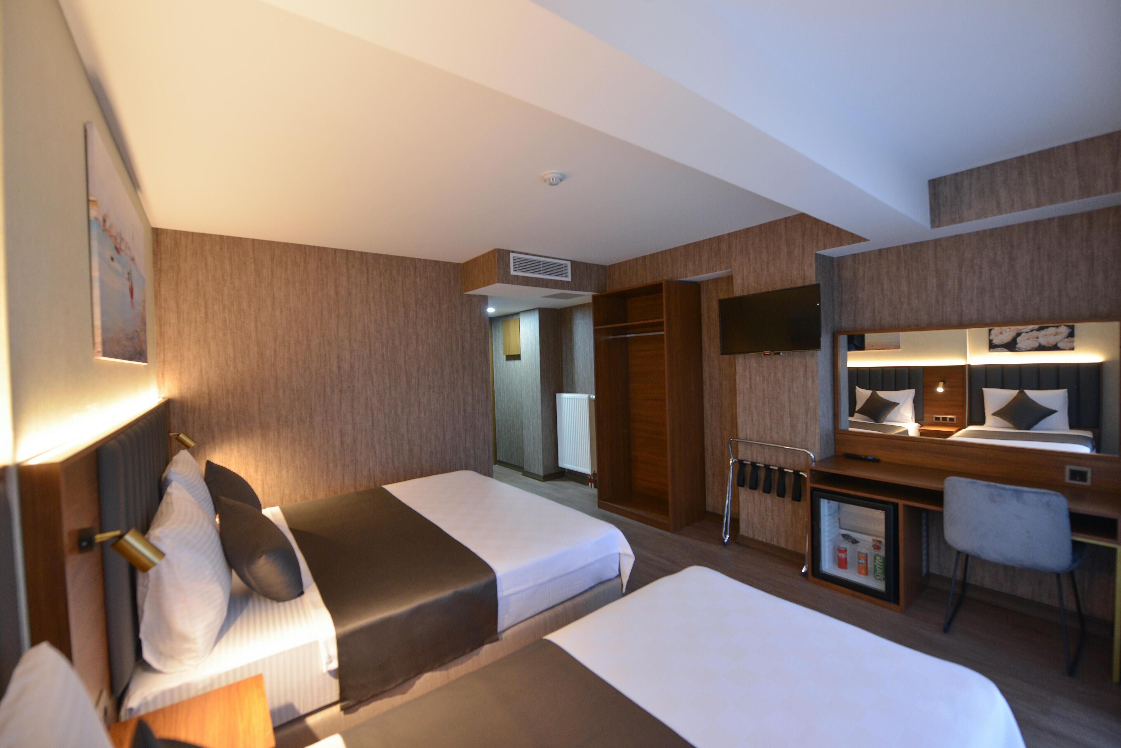 Ein Hotelzimmer mit zwei Betten, einem Schreibtisch, einem Stuhl, einem Fernseher und einem kleinen Schrank.