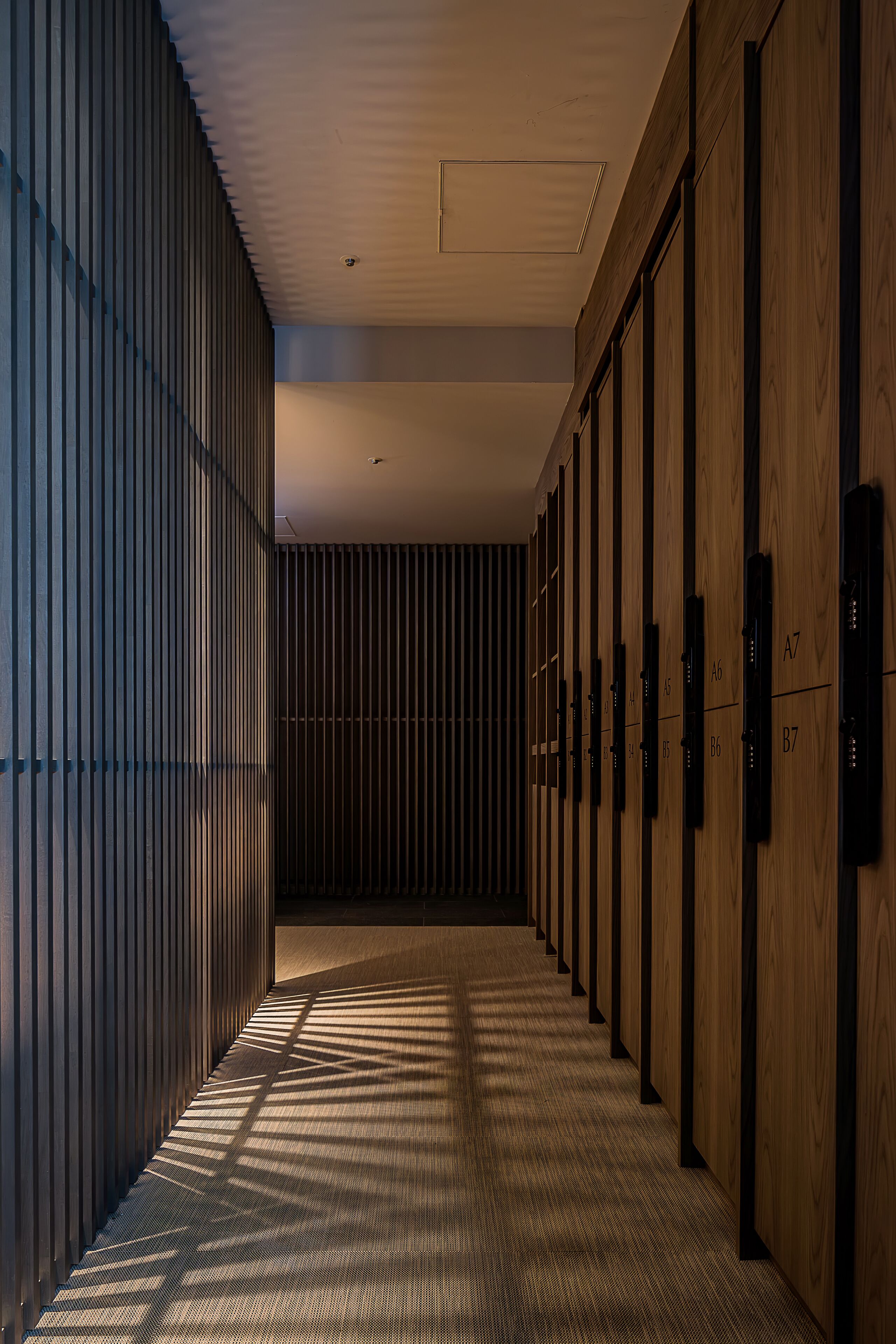 A corridor with wooden lockers and a patterned floor, leading to a room with a sloped ceiling and a light fixture.