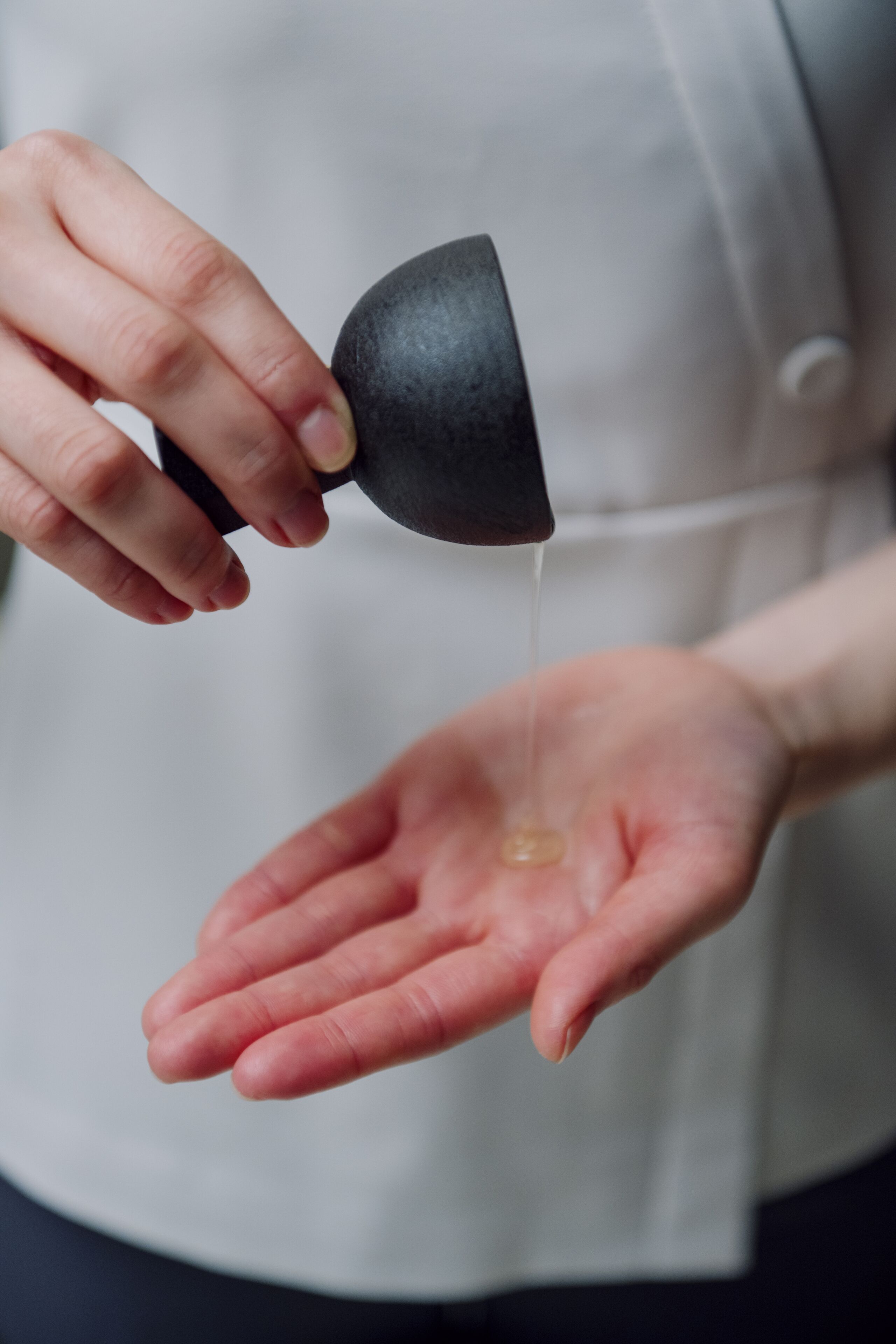 A person squeezing a liquid from a black container into their hand.