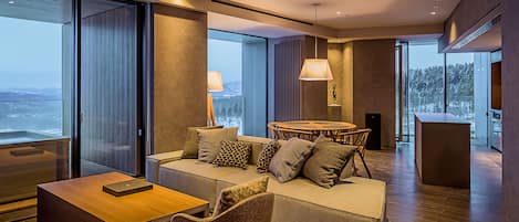 A modern living room with a sofa, armchairs, a wooden coffee table, and a dining area with a round table and chairs.