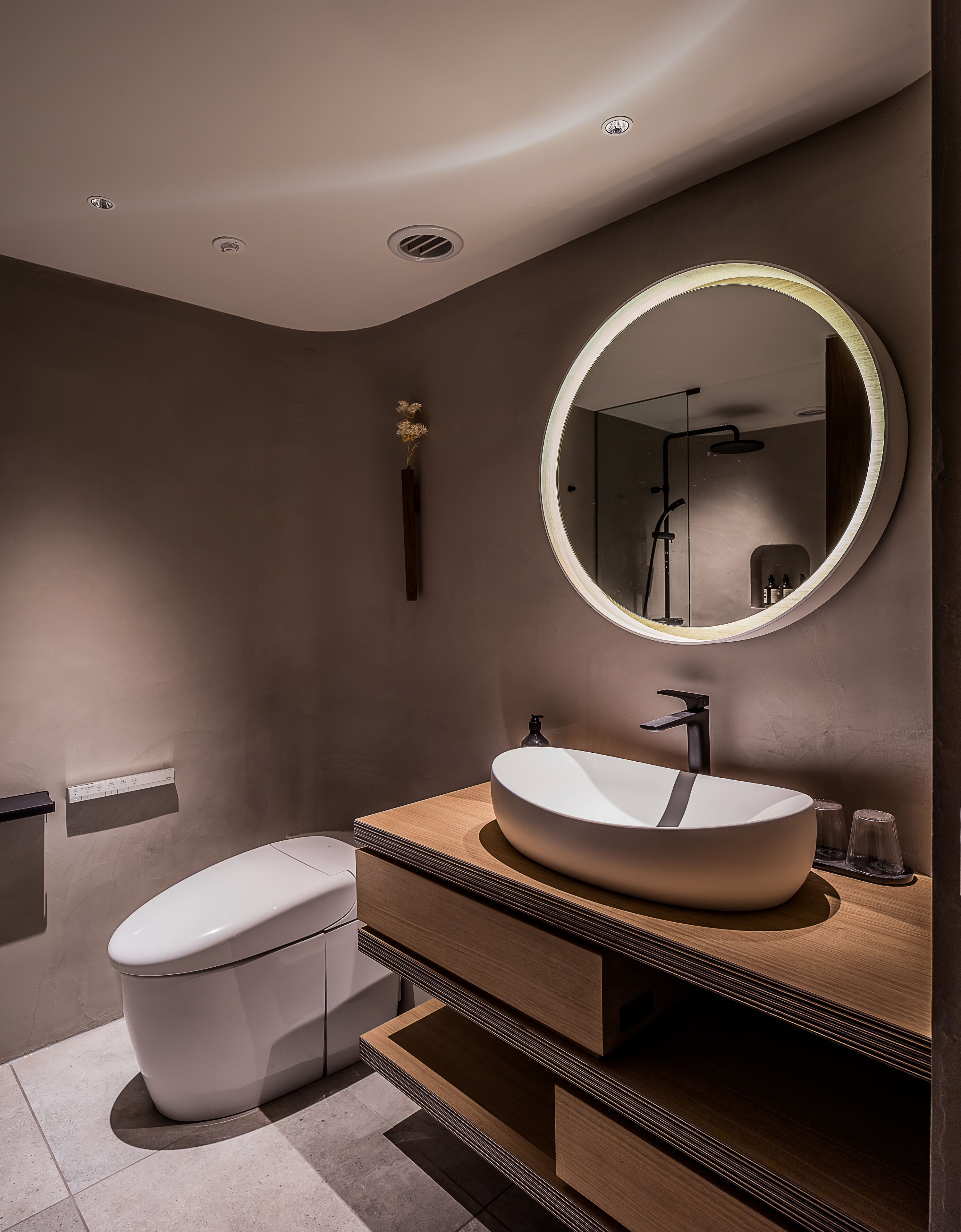 Une salle de bain moderne avec un miroir rond, un lavabo blanc et des toilettes.