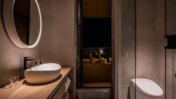 A modern bathroom with a large oval mirror, a wooden vanity, a white sink, and a toilet.