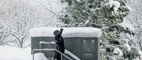 A person skiing on a snowy platform with a railing, surrounded by snow-covered trees.