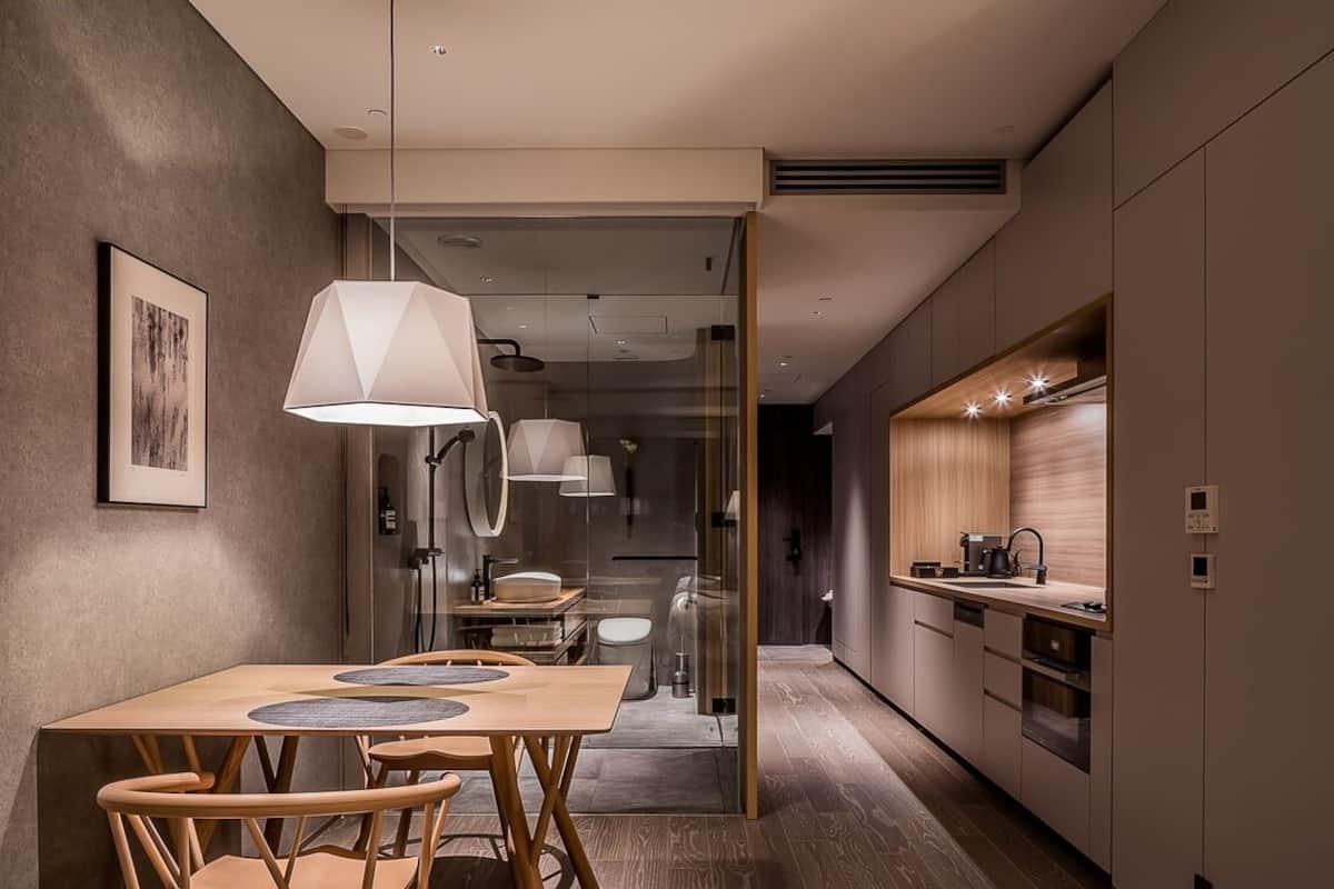 Una cocina moderna con comedor, que incluye una mesa y sillas, una lámpara colgante y vista al baño contiguo.