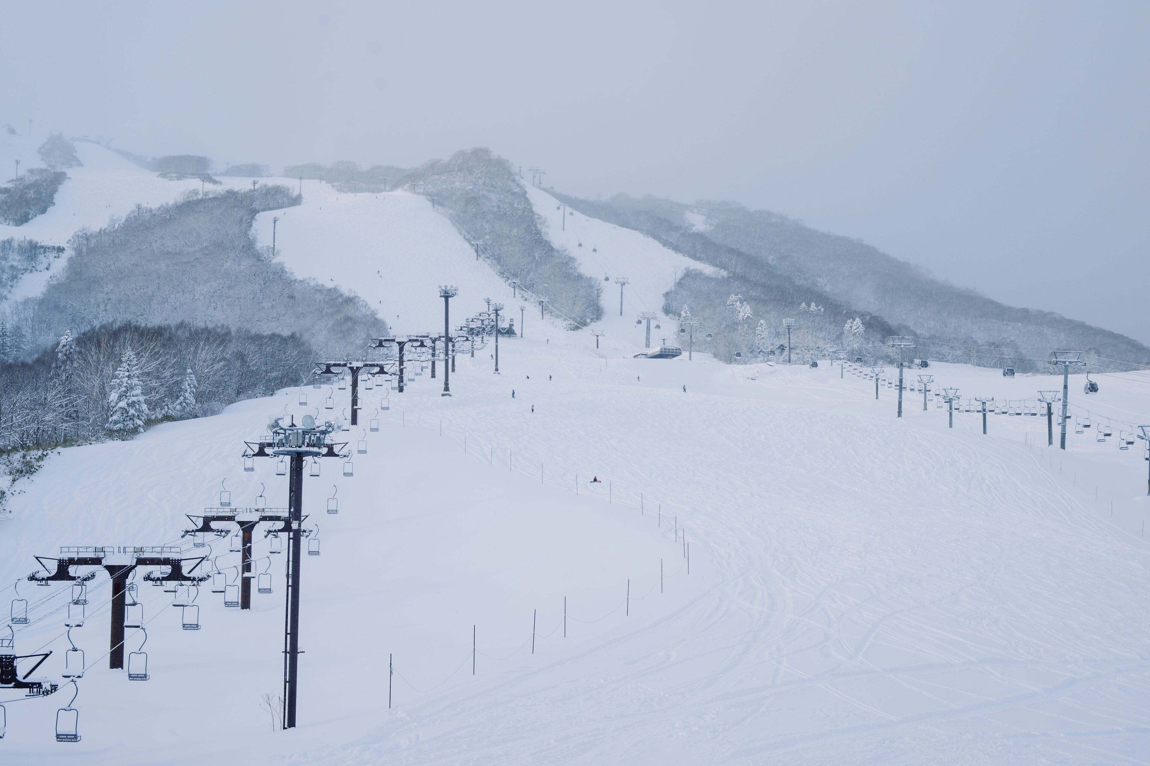 A snow-covered ski slope with ski lifts and a mountain backdrop.