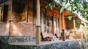 A wooden cabin with a stone foundation, large windows, and a porch with two chairs. - Ubuntu Bali Eco Yoga Retreat (Tibubeneng)