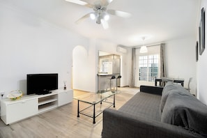 A modern living room with a flat-screen TV, glass coffee table, sofa, and dining area with chairs.