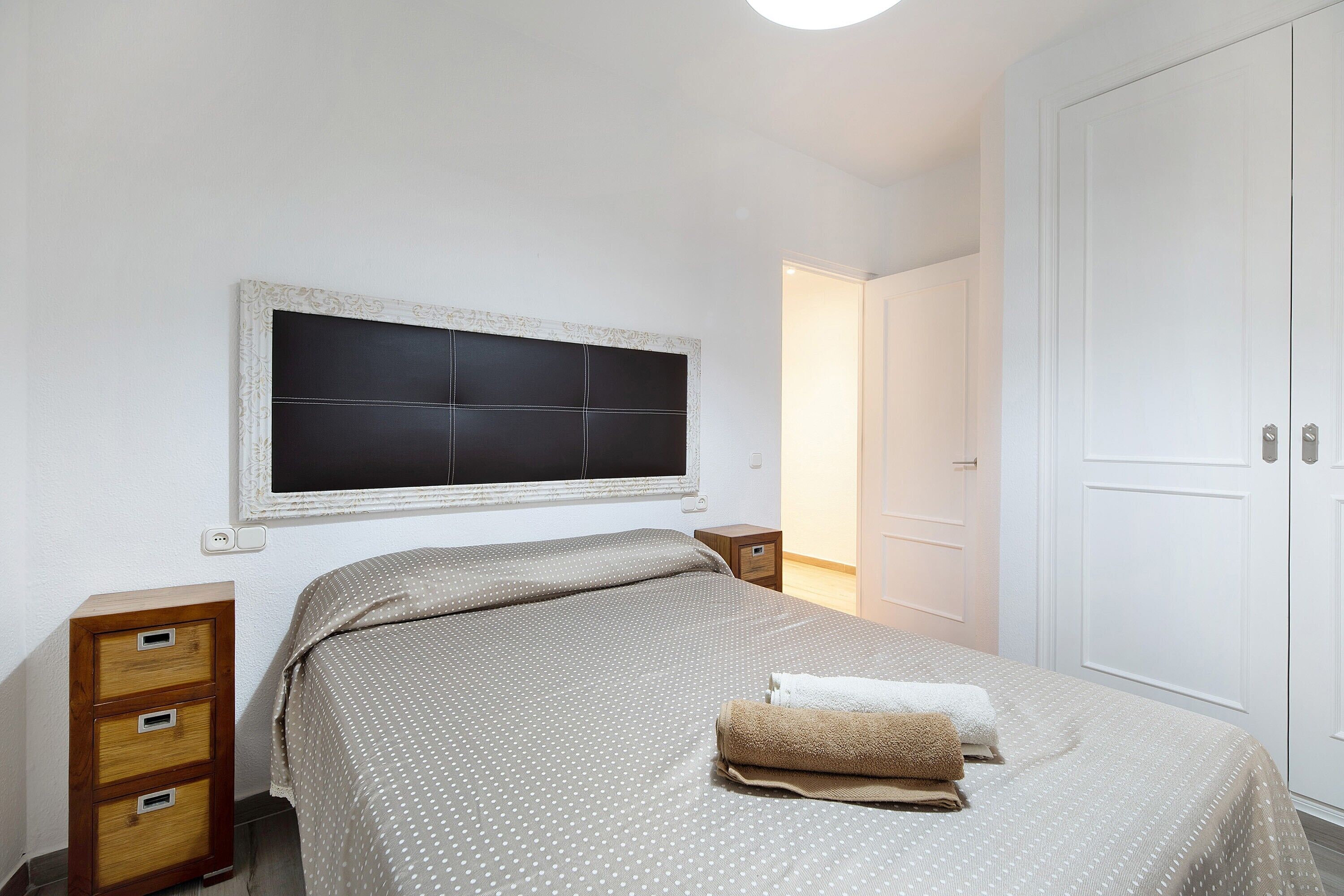 Un dormitorio con cama, mesita de noche, cómoda, ventana y puerta.