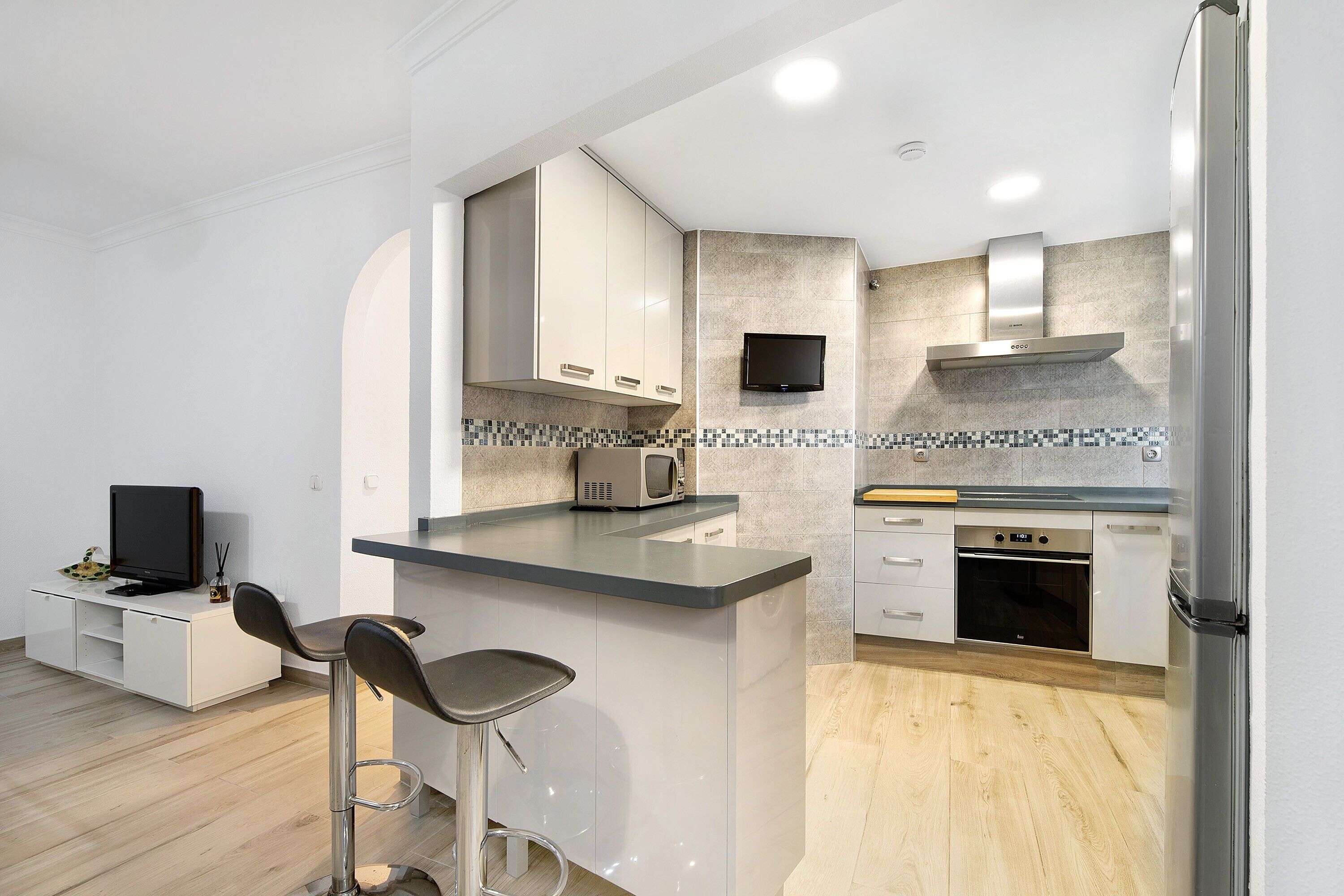 A modern kitchen with a bar area, built-in appliances, and a flat-screen TV.