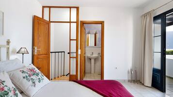 Een slaapkamer met een bed, een houten deur, een badkamer met een wastafel en uitzicht door een raam.