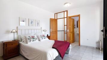 Un dormitorio con cama, mesita de noche y puerta de madera que da a otra habitación.