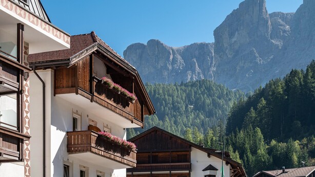 A building with wooden balconies, a mountain backdrop, and a clear sky. - Apartment "Stoffelapartments - Marie" with Mountain View, Shared Terrace & Wi-Fi (Wolkenstein)