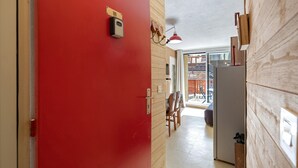 A hallway with a red door, a wooden wall, a hanging light fixture, and a view of an outdoor area with a wooden fence. - Apartment 'Le Relais Du Devoluy' with Mountain View and Terrace (Le Dévoluy)