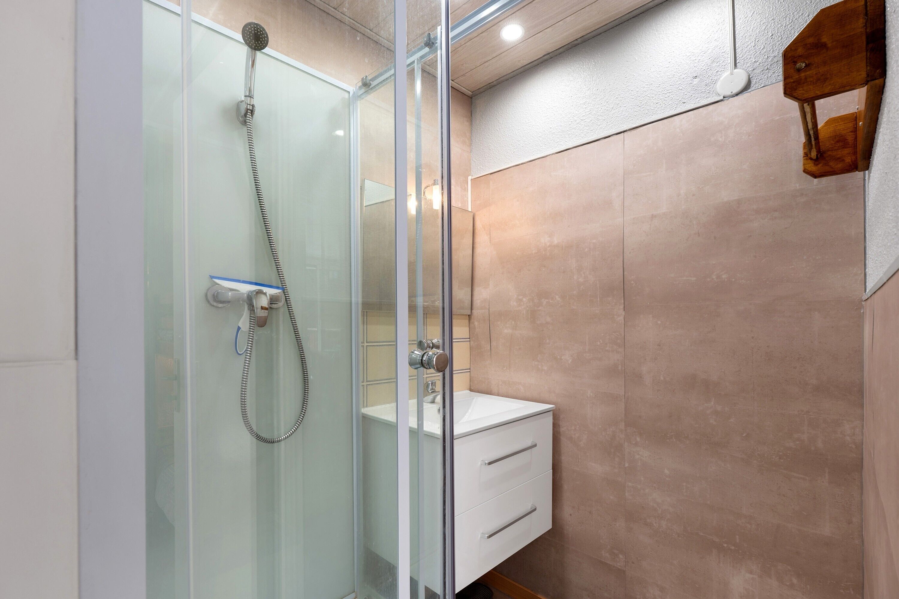 Une salle de bain moderne avec une douche à parois de verre, un lavabo blanc et un élément décoratif en bois sur le mur.