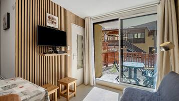 Een moderne woonkamer met een flatscreen televisie, een wand van houten panelen en een schuifdeur naar een buitenruimte met een tafel en stoelen.