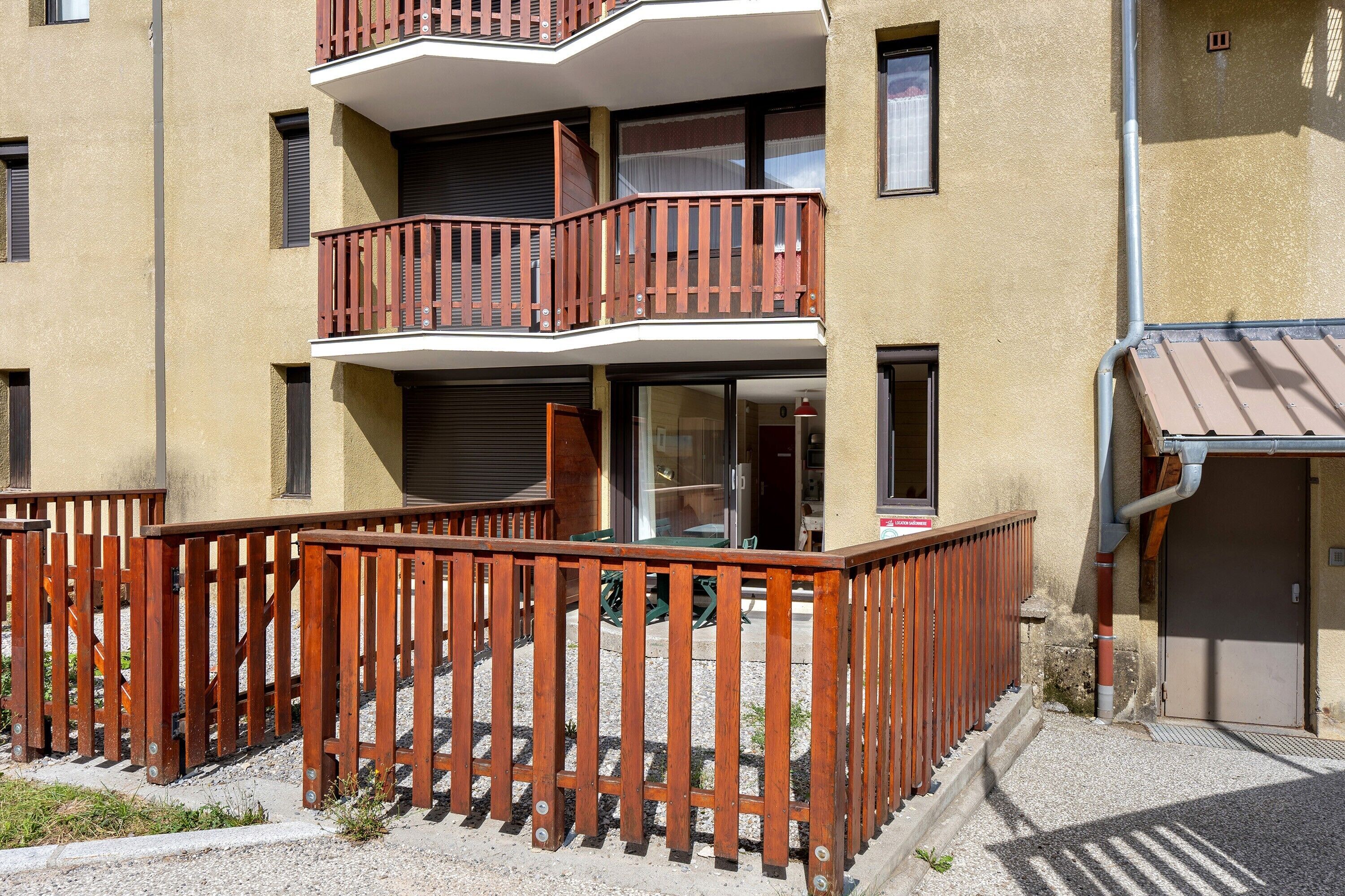 Un immeuble à plusieurs étages doté d’un balcon en bois et dont le sol est recouvert de gravier.