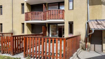 Un immeuble à plusieurs étages doté d’un balcon en bois et dont le sol est recouvert de gravier.