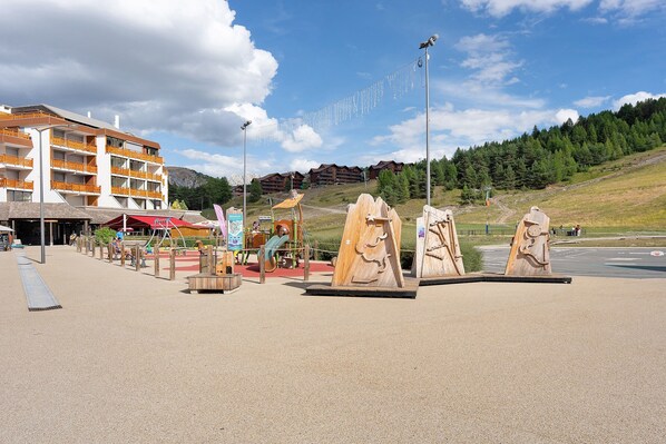 A playground with wooden climbing structures and a building with balconies in the background. - Apartment 'Le Relais Du Devoluy' with Mountain View and Terrace (Le Dévoluy)