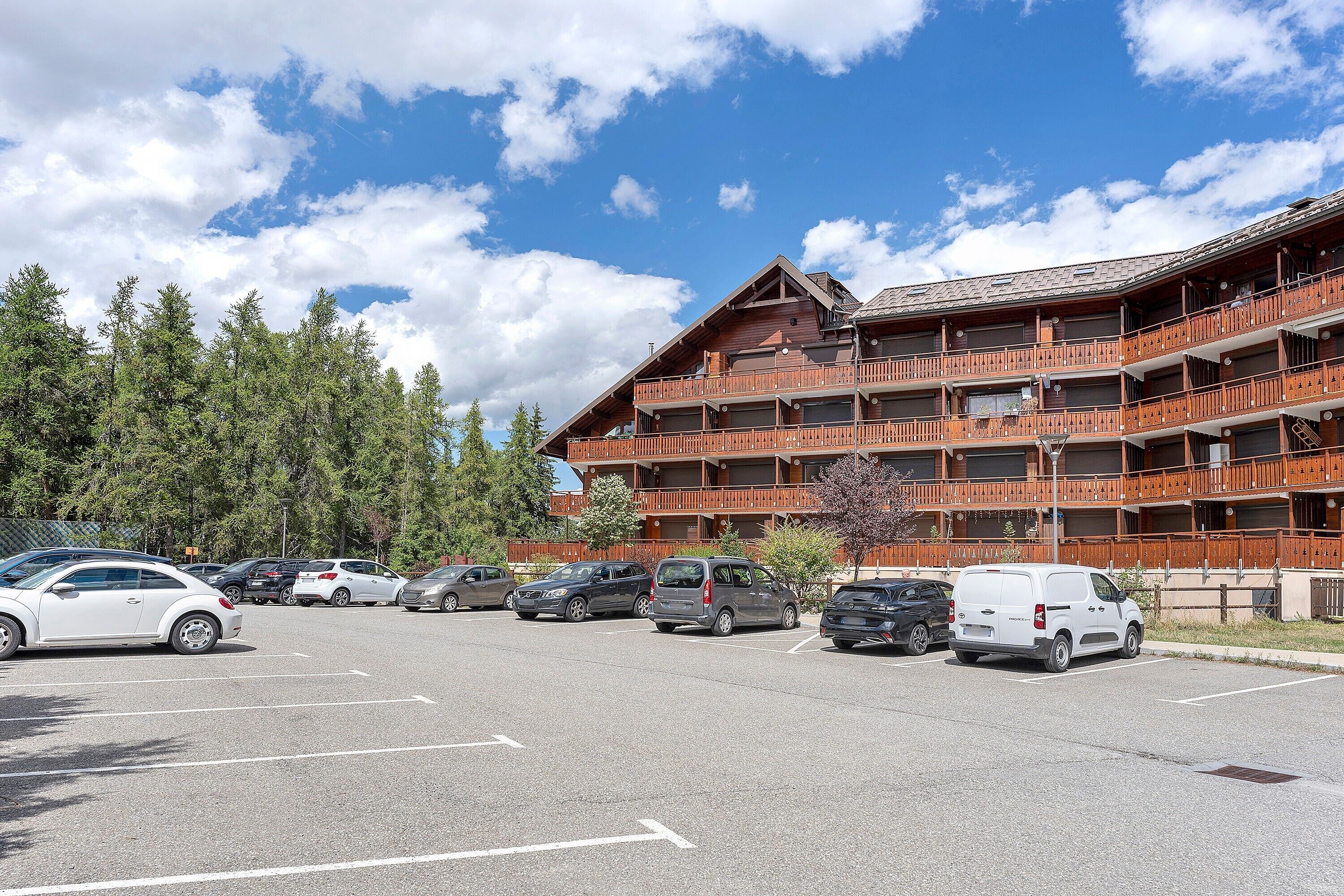 Un hôtel à plusieurs étages, doté d’une façade en bois, d’un parking et entouré d’arbres.