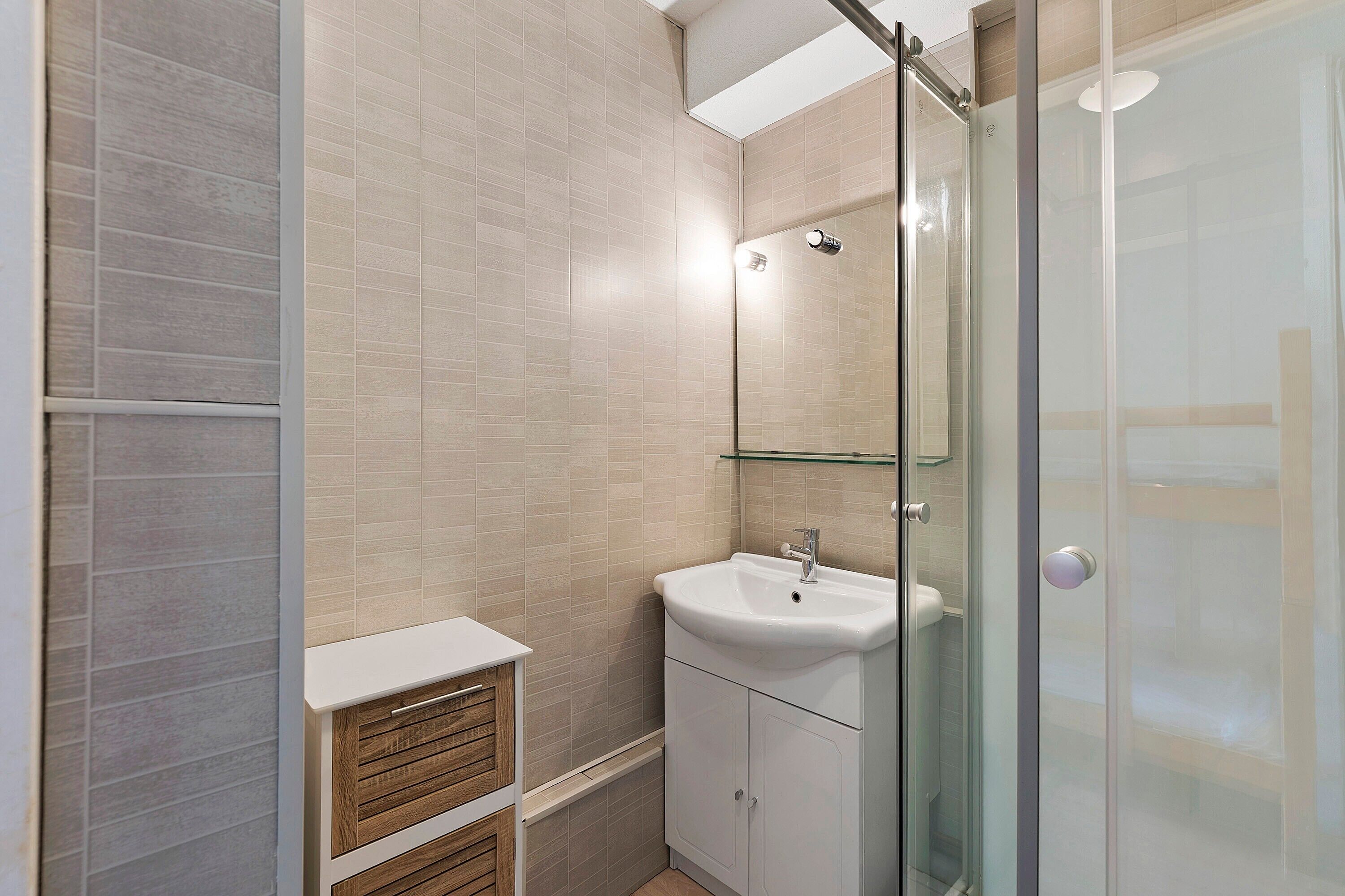Une salle de bain avec une douche à parois de verre, un lavabo blanc et un miroir au-dessus.