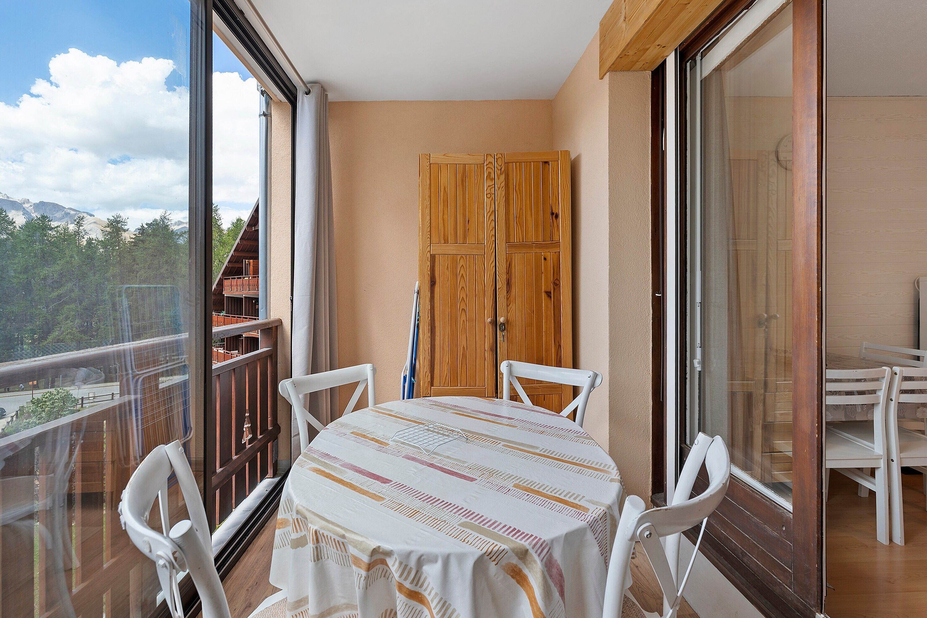 Un balcon avec une table et des chaises, une porte en bois et une vue sur une montagne.