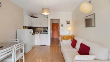 A compact living space with a kitchenette, a dining area, and a sofa with red cushions.