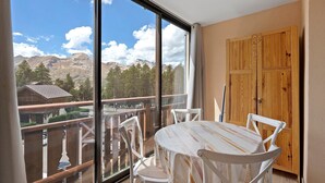 A balcony with a table and chairs, a wooden door, and a mountain view. - Studio Apartment "Les Fontettes 2" near Slopes with Balcony & Shared Pool (Le Dévoluy)