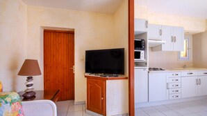 Un espace de vie compact comprenant un coin cuisine, un téléviseur, un coin repas avec une table et des chaises, et une porte donnant sur une autre pièce.