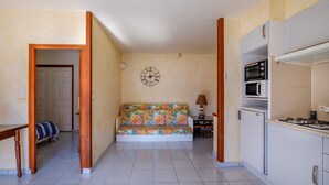 Une pièce comprenant un canapé, une table à manger, une lampe, une horloge et des appareils de cuisine.
