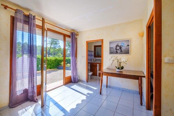 A room with a sliding glass door leading to a garden, a wooden table with a potted plant, and a framed picture on the wall.