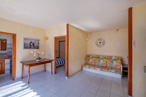A room with a sofa, a table with a plant, a clock on the wall, and a door leading to another room. - Holiday Apartment '4 Personnes Le Tignet' with Pool, Shared Garden and Wi-Fi (Le Tignet)