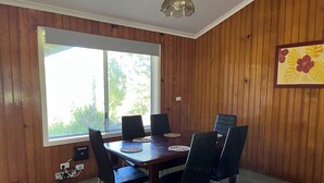 Comedor con mesa y sillas de madera, un ventanal grande y una lámpara en el techo.