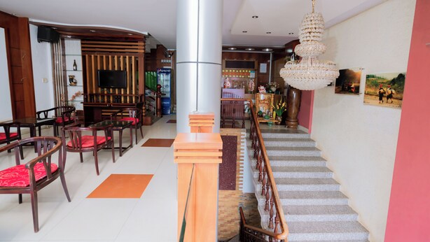A hotel lobby with a staircase, wooden furniture, a chandelier, and a television. - Trieu Vu Hotel & Apartment (Buon Ma Thuot)