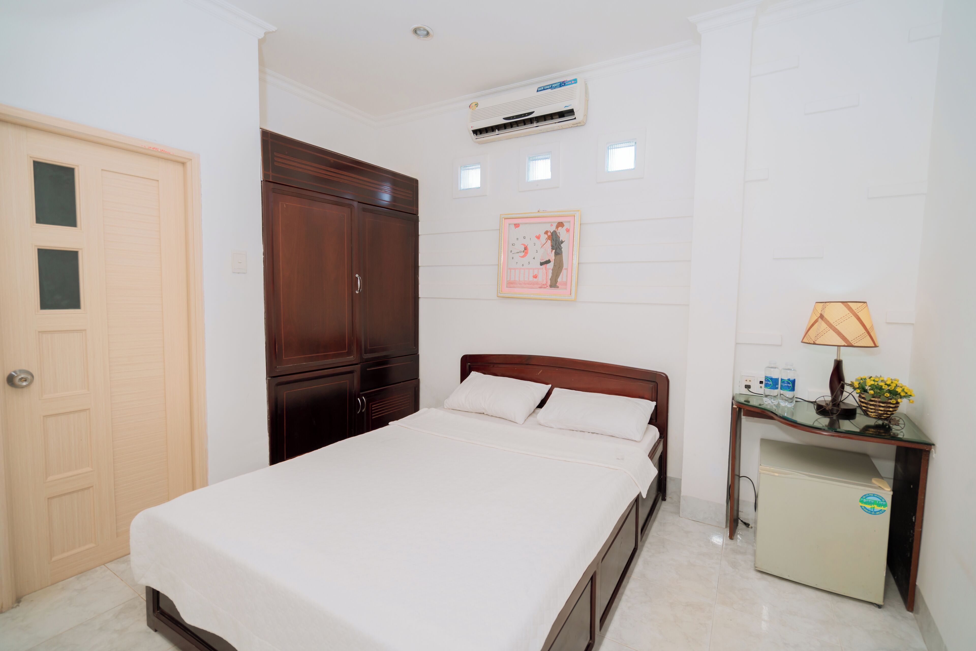 Un dormitorio ordenado con cama, armario, escritorio con lámpara y equipo de aire acondicionado en la pared.
