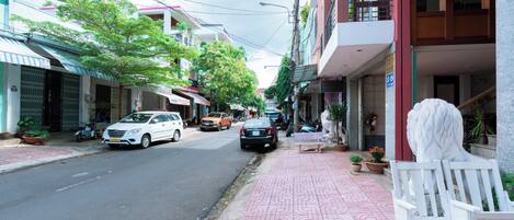 A street with parked cars, a sidewalk with a patterned pavement, and buildings with balconies and potted plants.