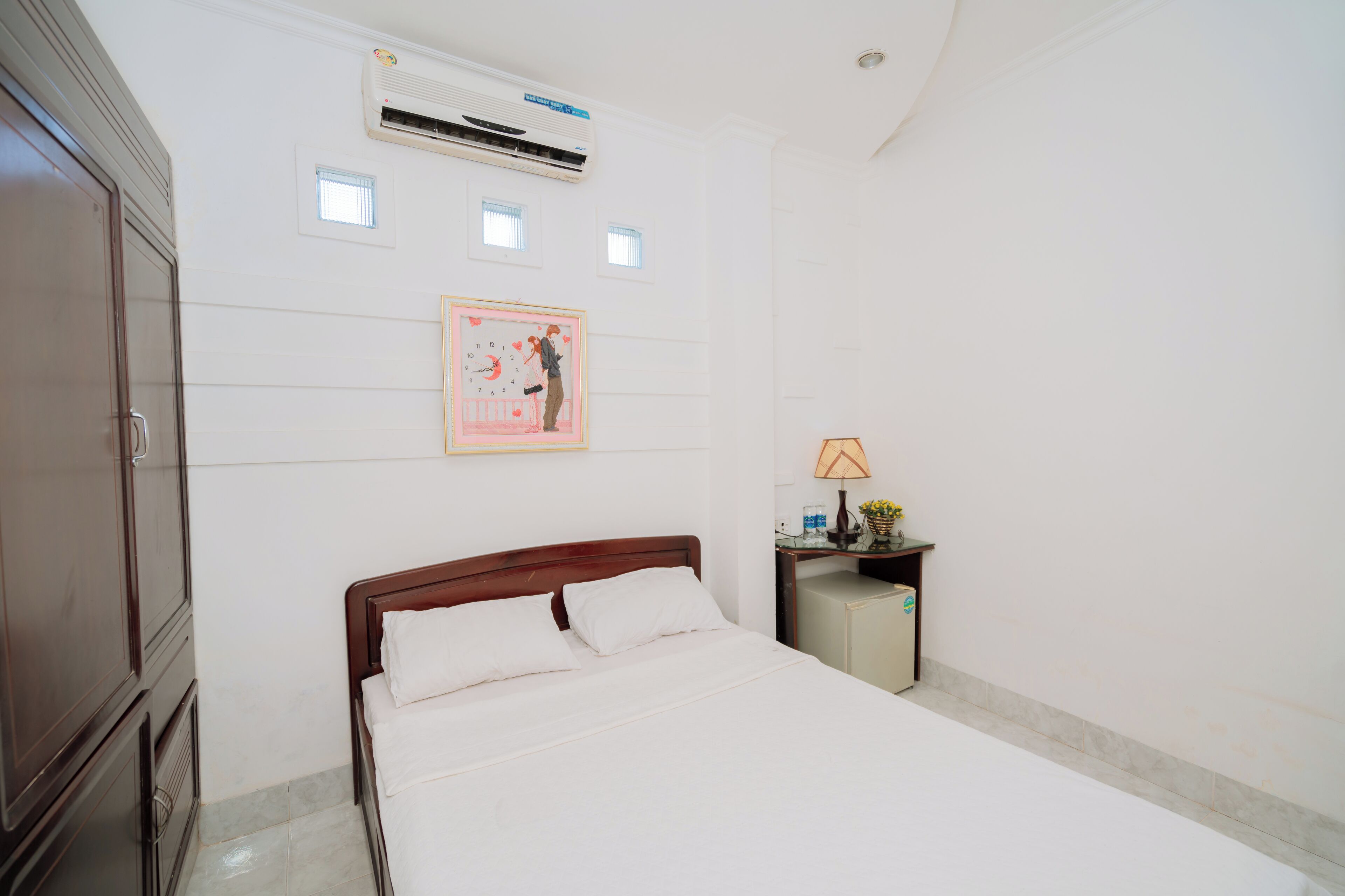 A hotel room with a bed, a nightstand, a lamp, and an air conditioning unit.