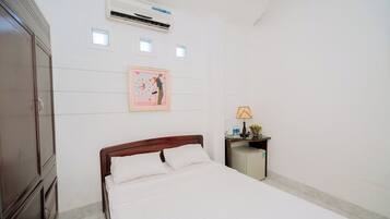 A hotel room with a bed, a nightstand, a lamp, and an air conditioning unit.