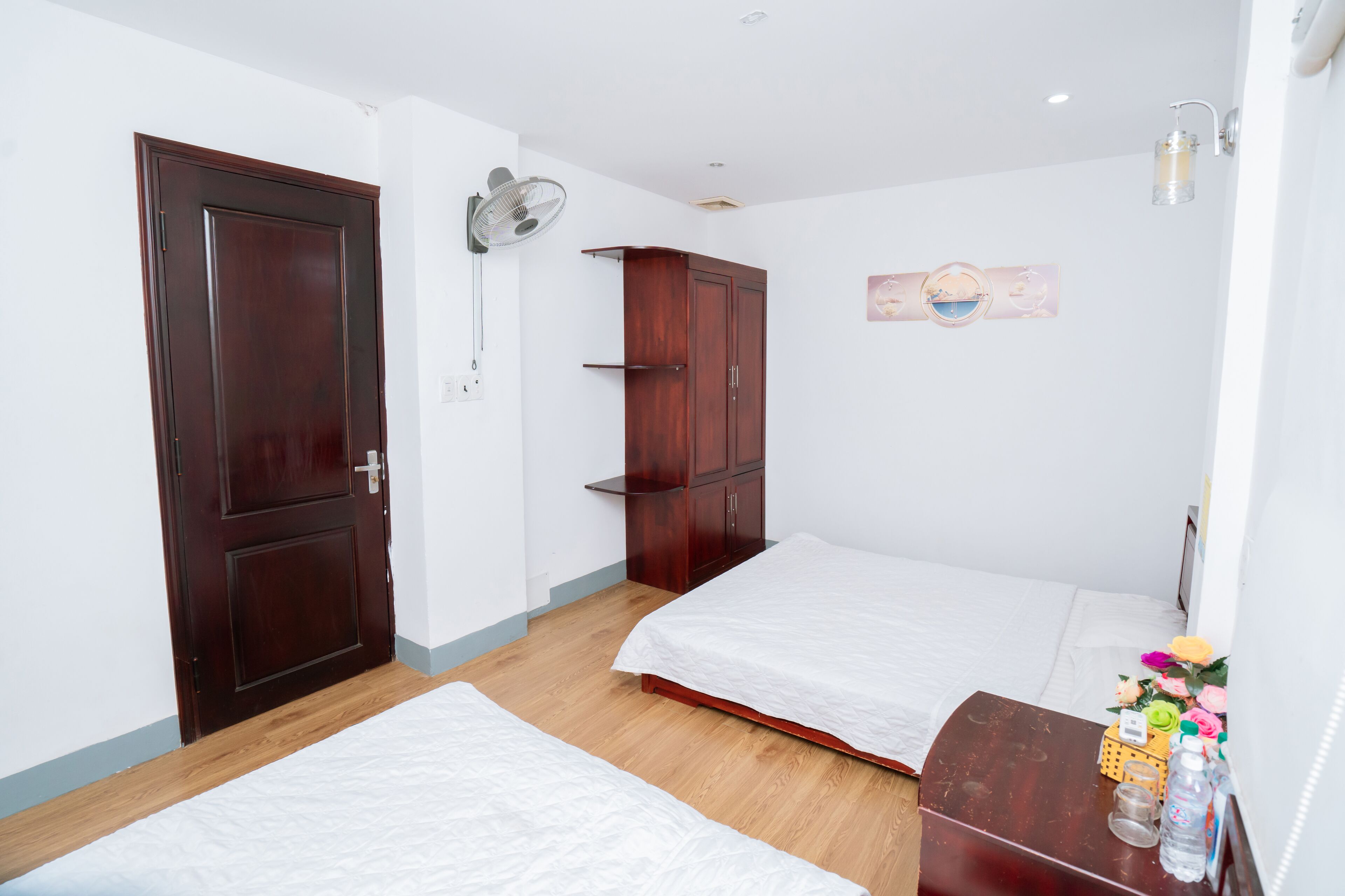 A bedroom with two beds, wooden wardrobe, and a bedside table with a lamp.