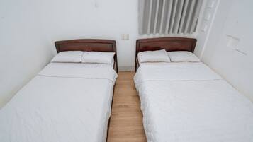 Ett rum med två separata sängar, sänggavlar i trä, vitt sänglinne och ett trägolv.