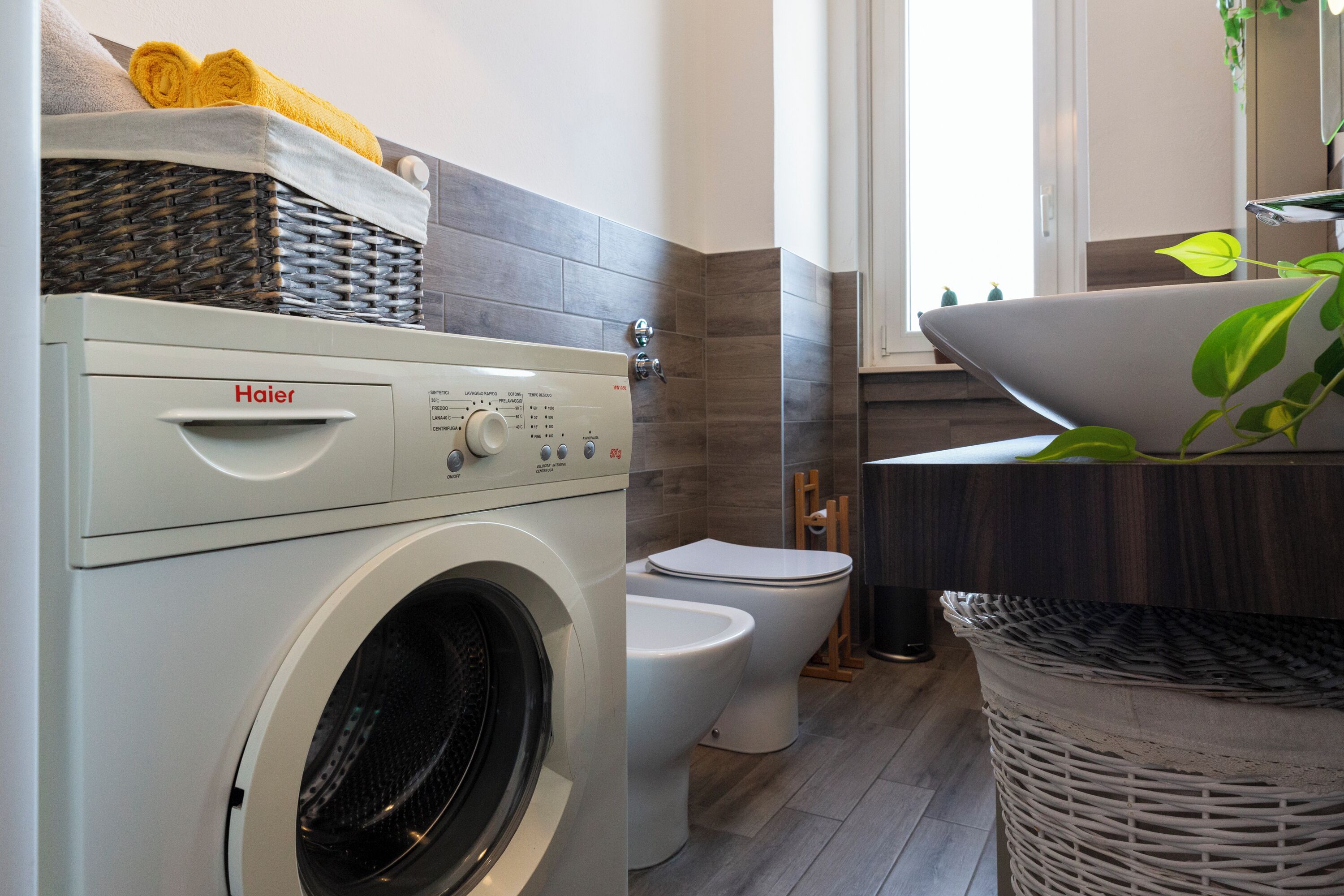 Ein modernes Badezimmer mit einer Haier Waschmaschine, zwei Toiletten, einem Waschbecken und einem Korbwäscheschrank.