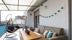 En balkong med en hängstol, en soffa och ett träbord.