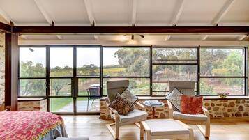 A spacious room with large windows, a bed, two armchairs, and a small table.