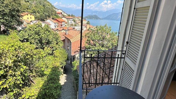 Un balcon donnant sur un lac et des maisons, avec une rambarde en métal et une porte équipée de volets.
