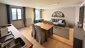 Un salon moderne avec une table à manger en bois, un ensemble de canapés et une grande œuvre d’art abstraite accrochée au mur.