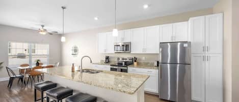 Cozinha moderna com ilha central, eletrodomésticos de aço inoxidável e armários brancos.