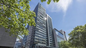 Un immeuble moderne de grande hauteur, doté d’une façade en verre, entouré d’arbres et d’autres bâtiments.