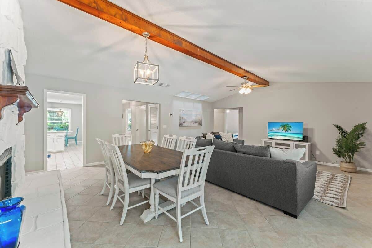 A spacious living area with a dining table, white chairs, a gray sofa, and a television.