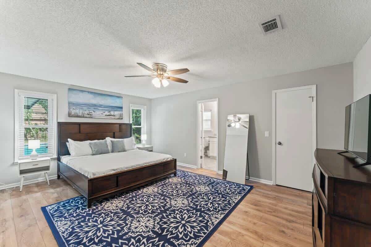 Une chambre à coucher comprenant un lit, un ventilateur de plafond, une fenêtre avec des stores, une porte et une commode.
