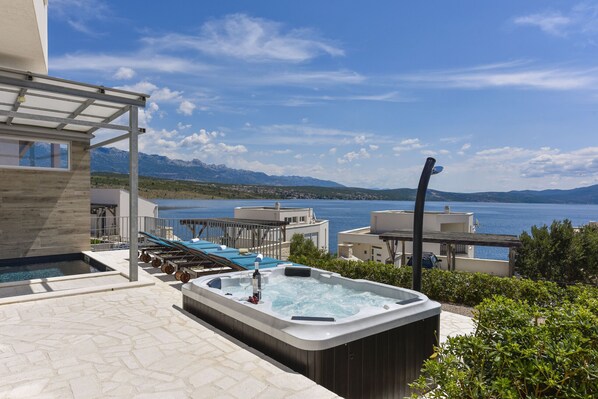Tagterrasse med pool, jacuzzi, liggestole og udsigt over hav og bjerge.
