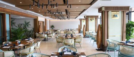 A spacious restaurant with high ceilings, modern pendant lighting, and a variety of seating options including tables and chairs.